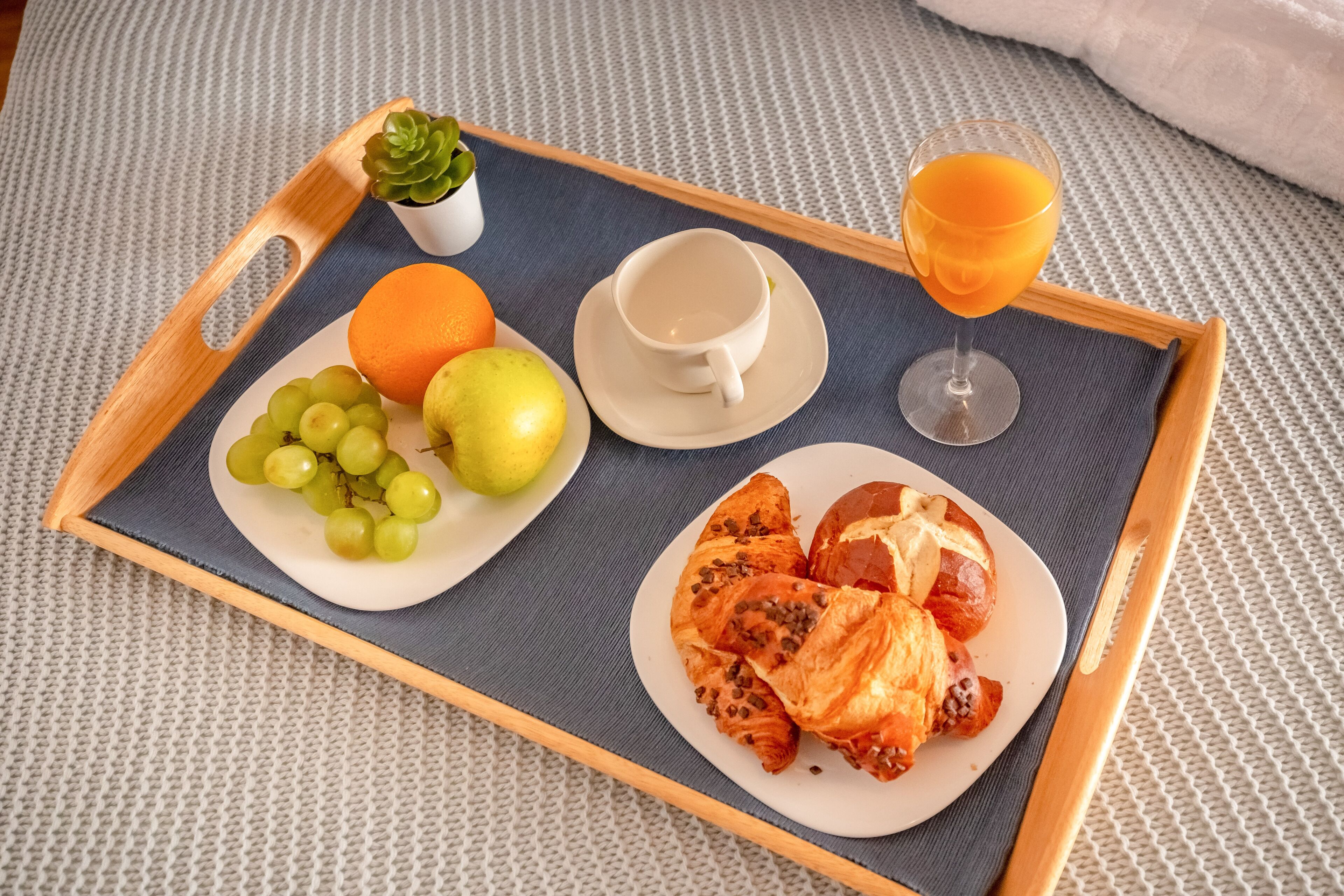 En bakke med mad og drikkevarer, blandt andet druer, en appelsin, pære, croissanter og et glas appelsinjuice.