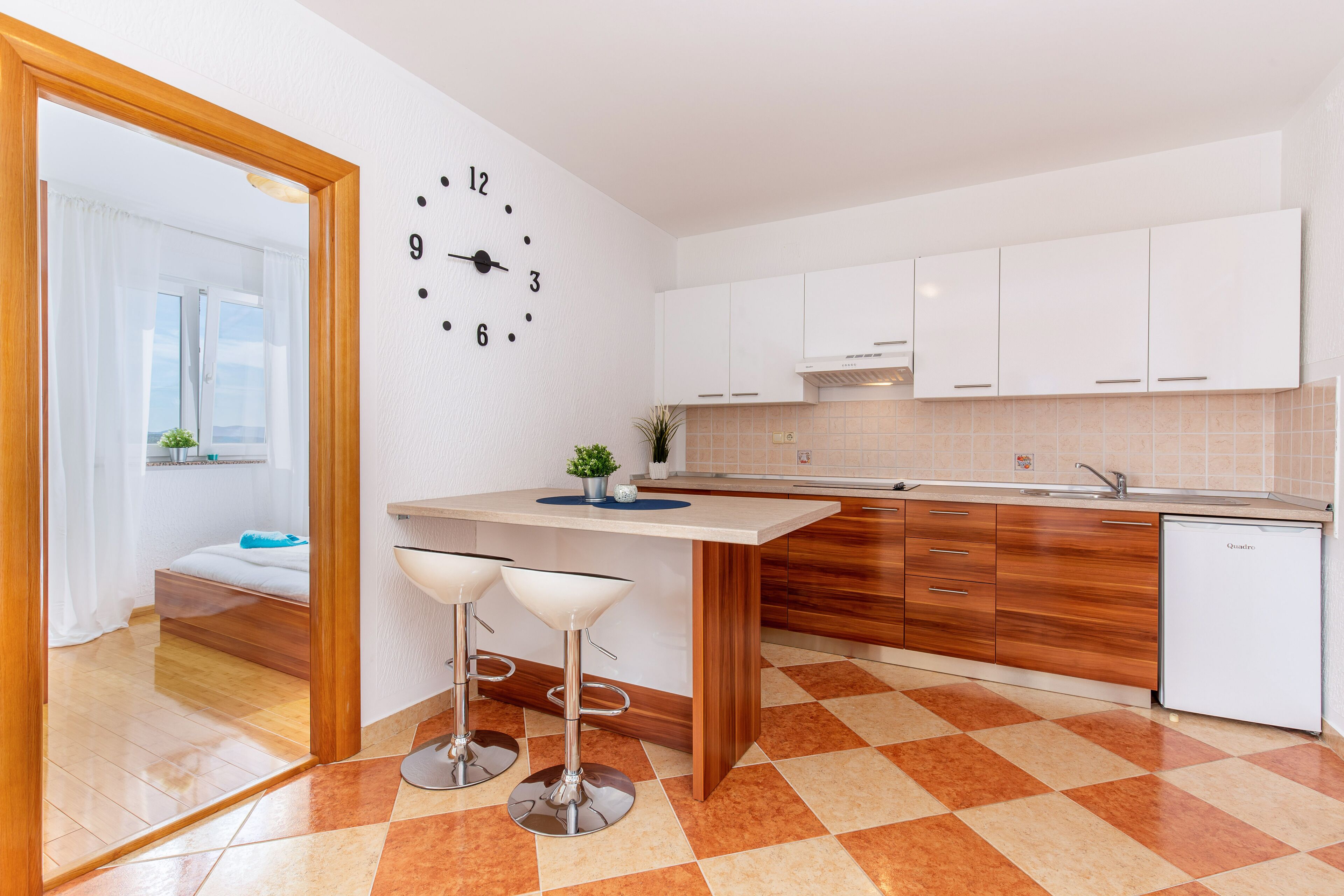 A modern kitchen with a clock, wooden cabinets, and a tiled floor.