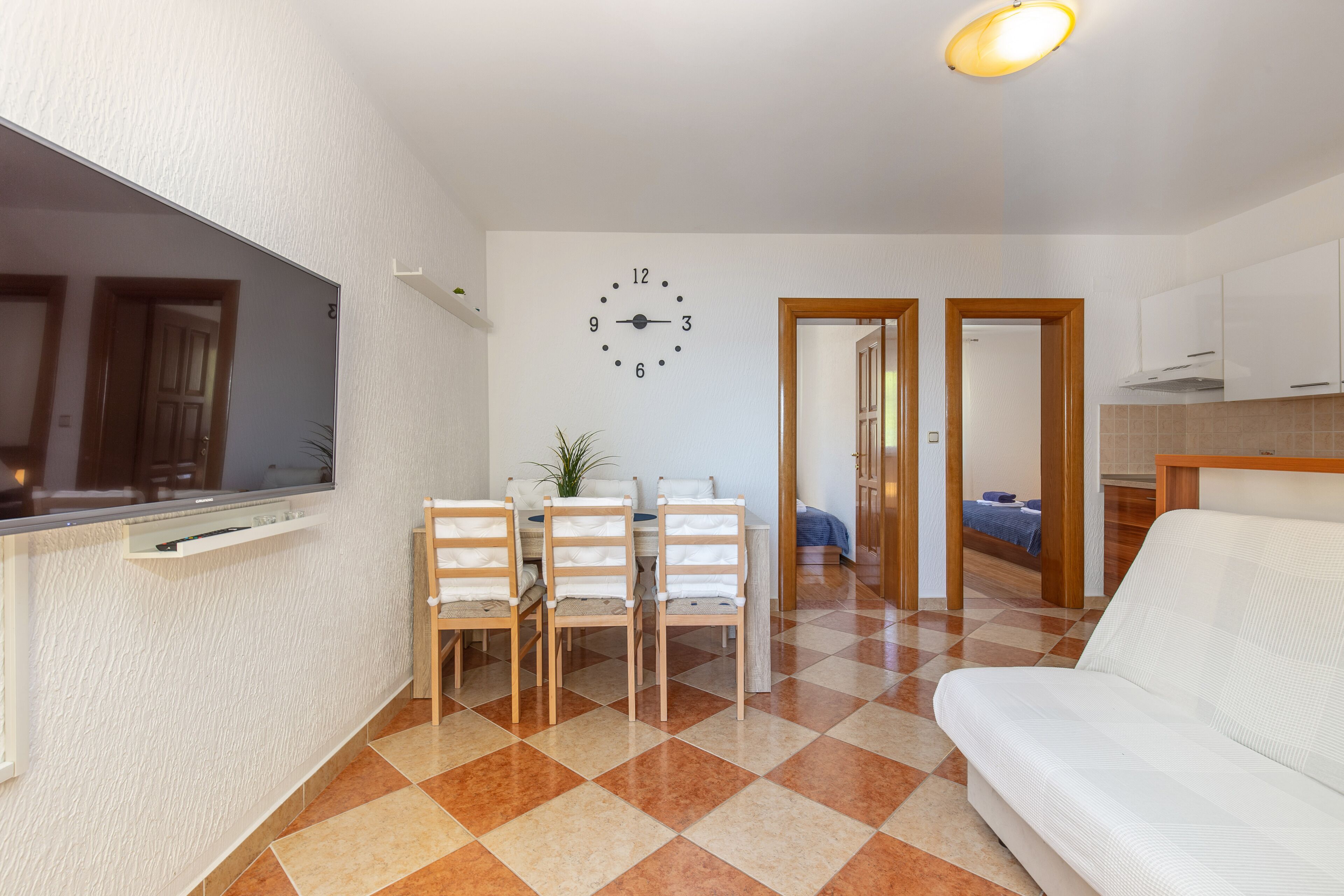 A compact living space with a dining area, a sofa, a clock, and a kitchen.