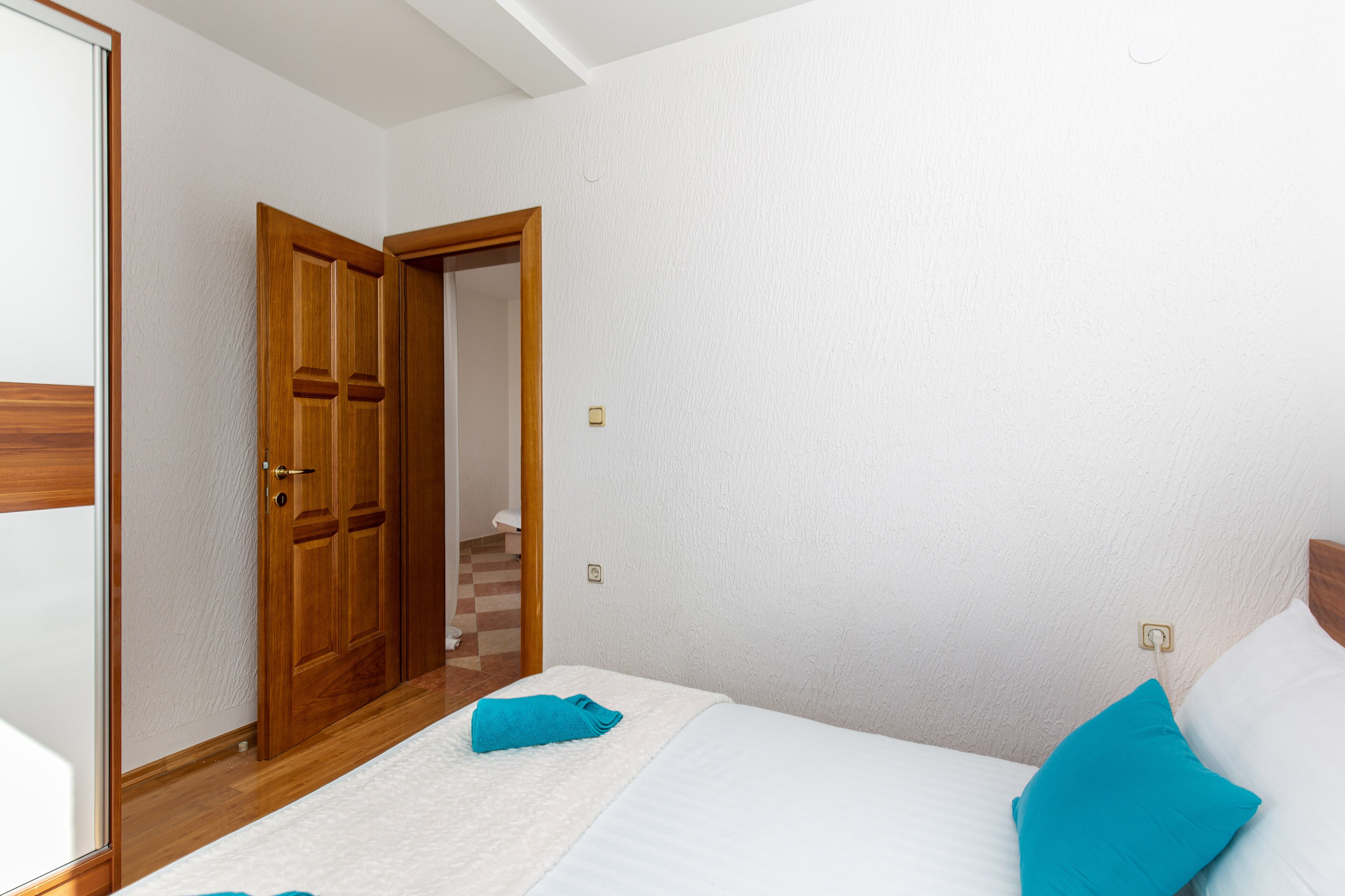A bedroom with a bed, a wooden door, and a white wall.