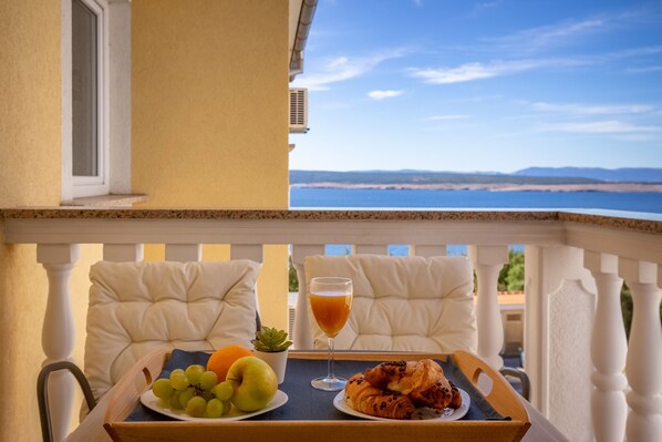 A balcony with a breakfast tray, a glass of orange juice, and a scenic view of the beach. - Villa Oleander (Crikvenica)