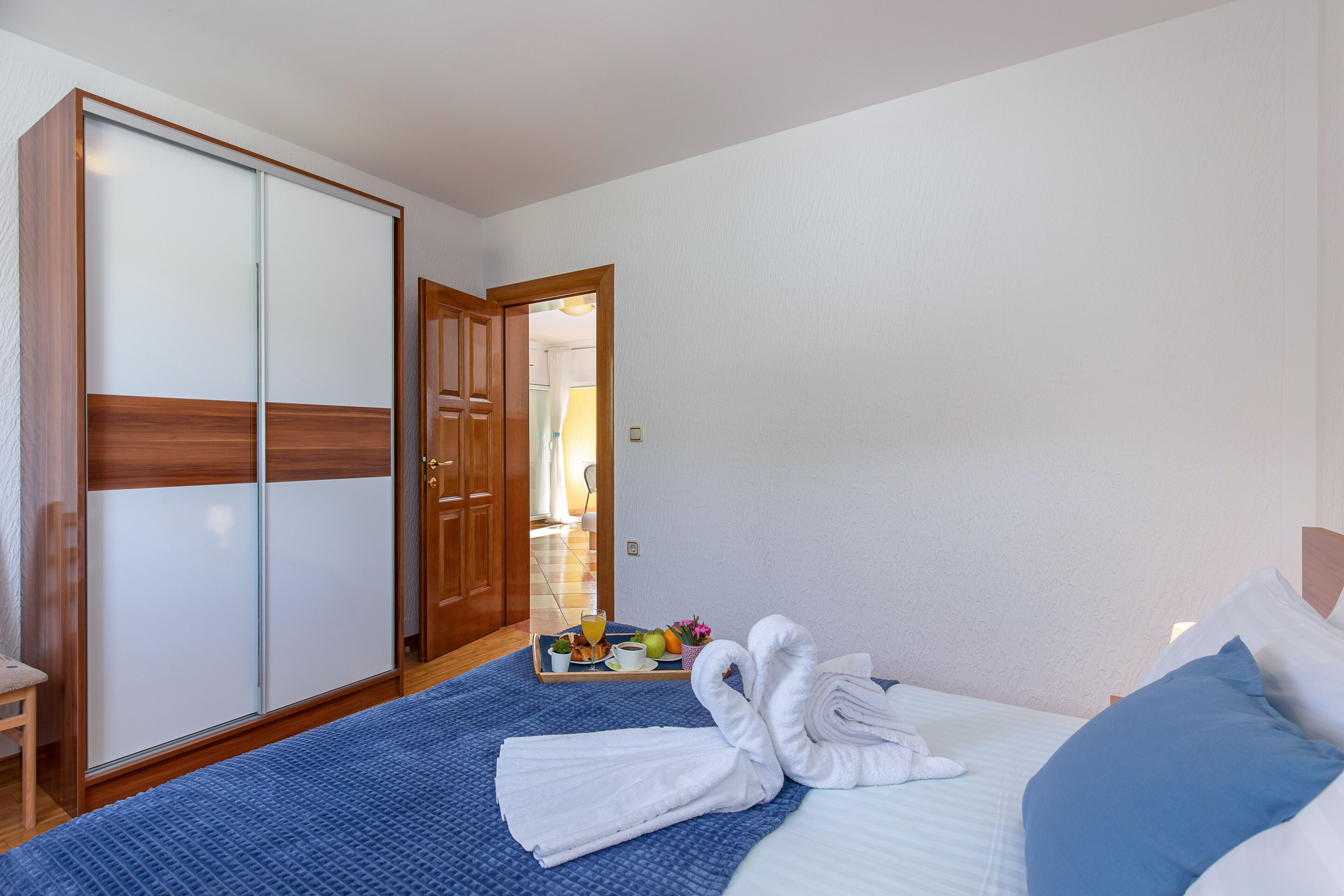 Habitación de hotel con cama, armario, bandeja con alimentos para el desayuno y baño visible a través de una puerta abierta.
