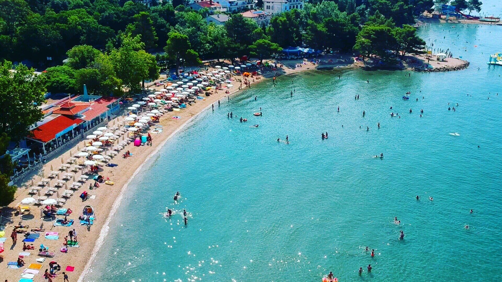 A beach with numerous umbrellas and people swimming.