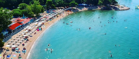A beach with numerous umbrellas and people swimming.