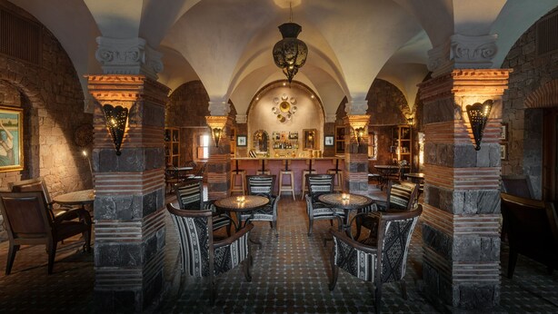 Ein historisches Interieur mit Säulen aus Stein, Gewölbedecken und einer zentralen Bar mit Sitzgelegenheiten.
