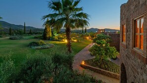 Ein gepflegter Garten mit einer Palme, ein Steinhaus mit Holzhörnern und freier Sicht auf ferne Berge.