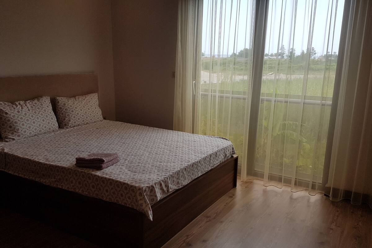 A bedroom with a bed, a window with curtains, and a view of the outdoors.