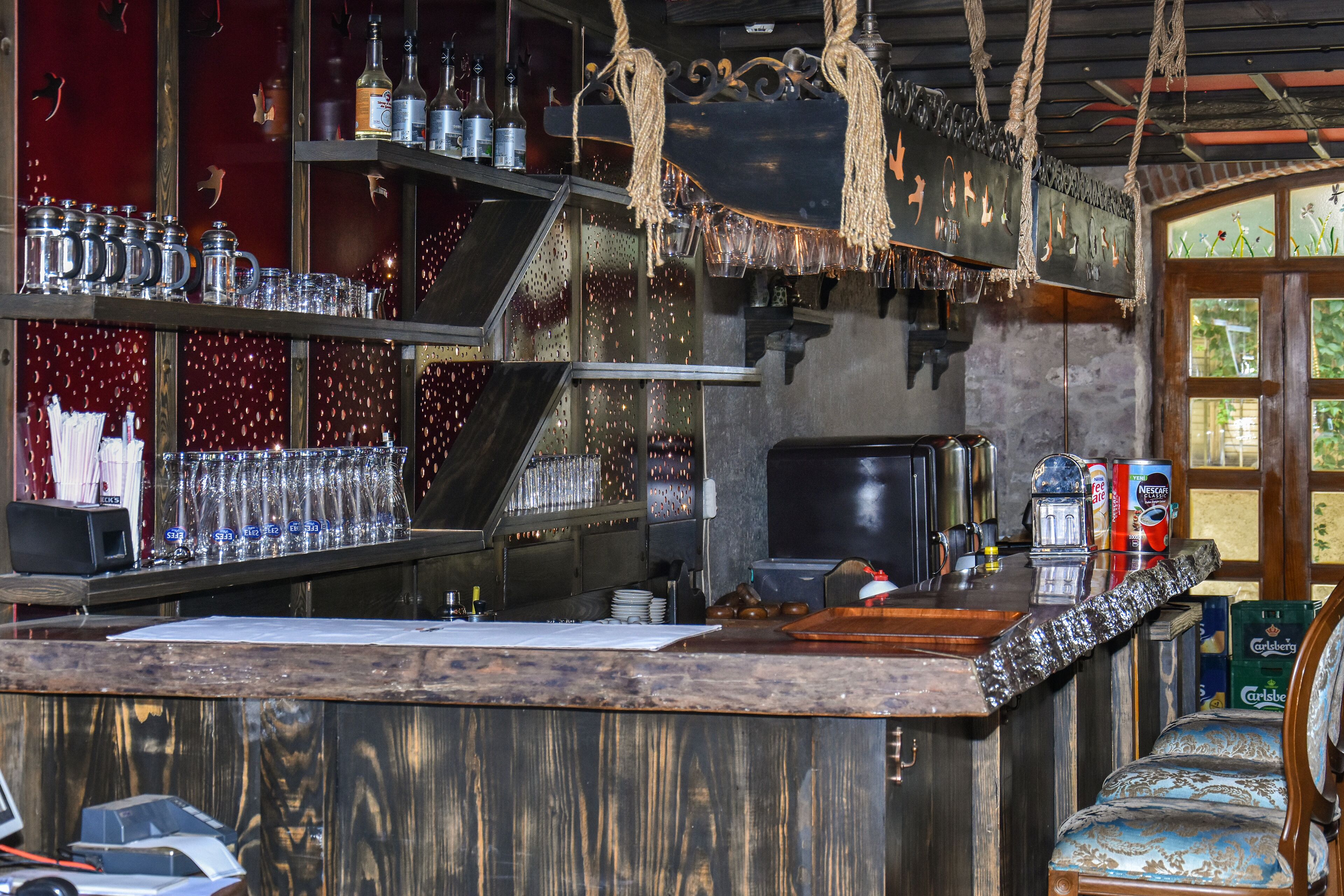Una zona de bar con estanterías llenas de botellas, vasos y una máquina de café.