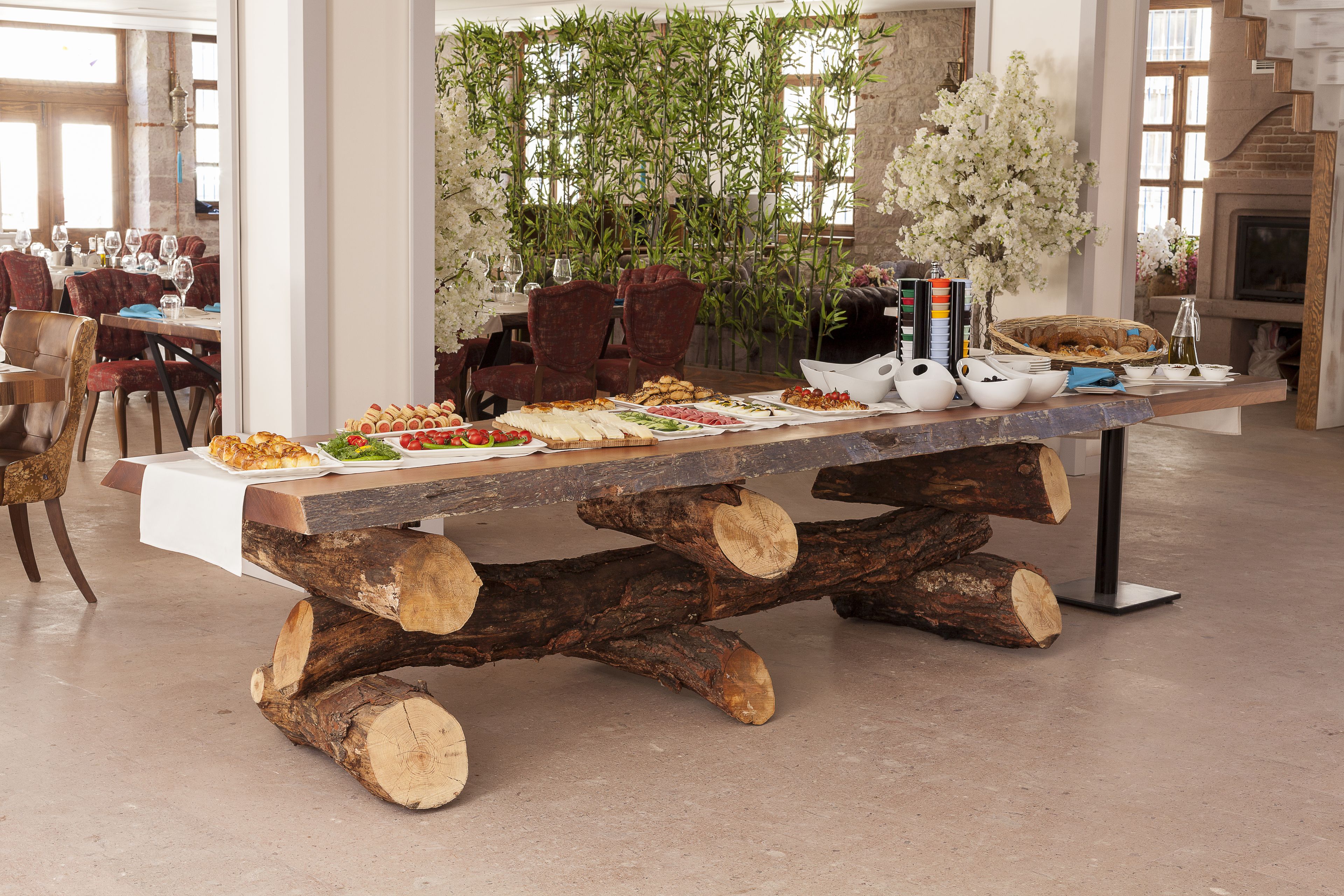 A dining table with a rustic log base, surrounded by chairs and a variety of food items.