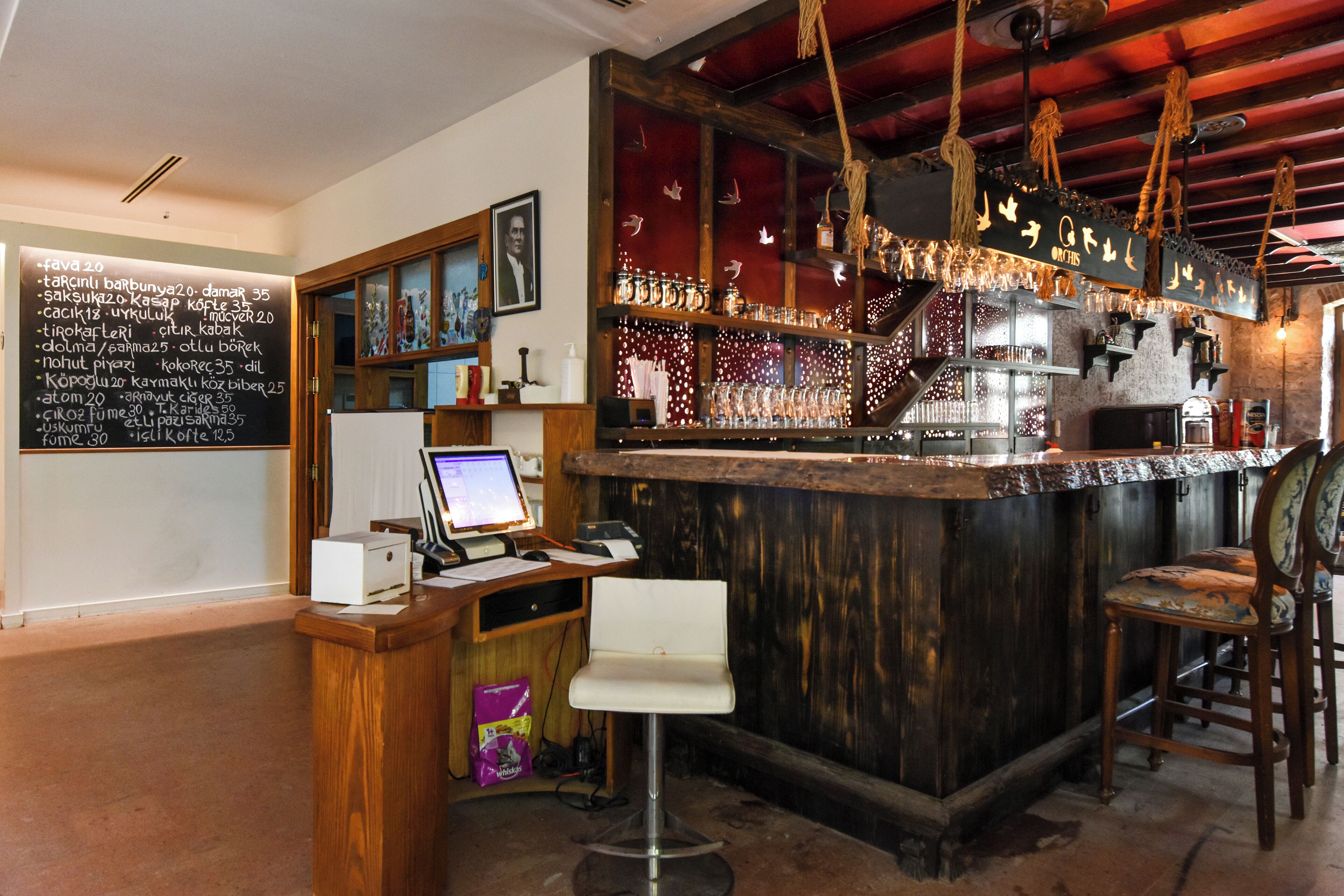 A bar area with a wooden counter, a computer, and a menu board.