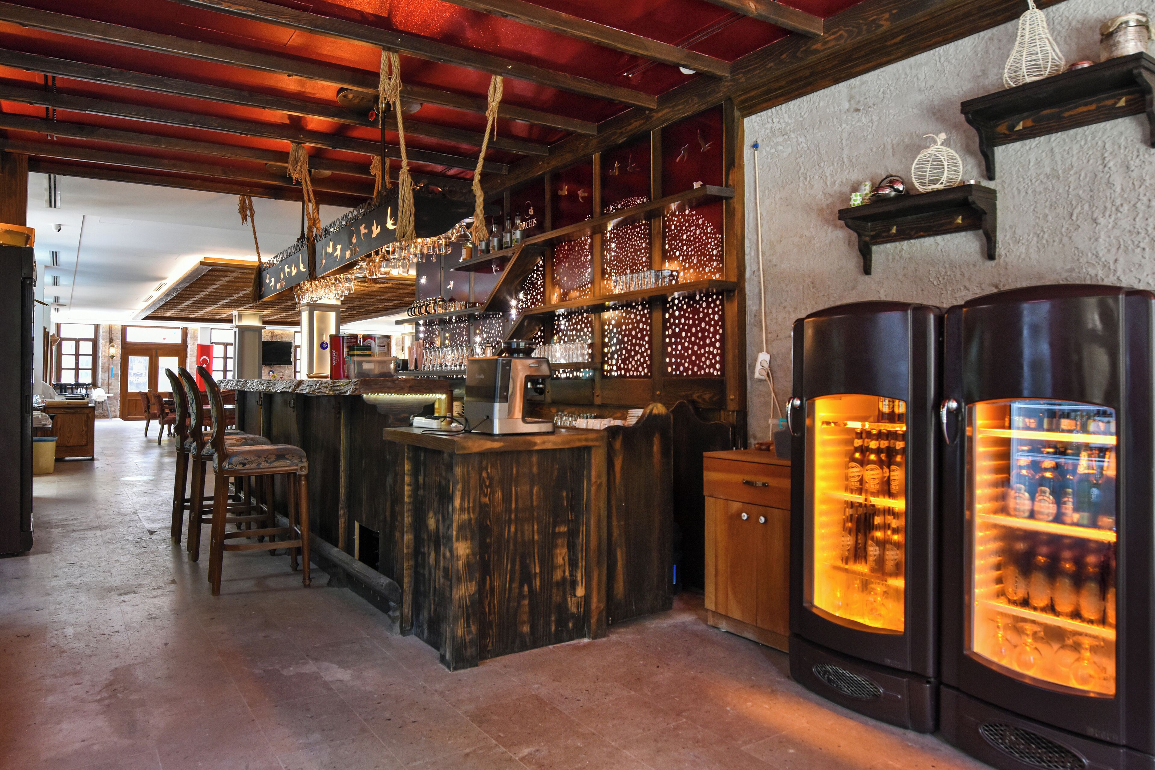 Zona de bar con mobiliario de madera, barra y un refrigerador grande con botellas.