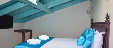 A hotel room with a bed, a wooden headboard, a nightstand, a wall-mounted TV, and a ceiling fan.