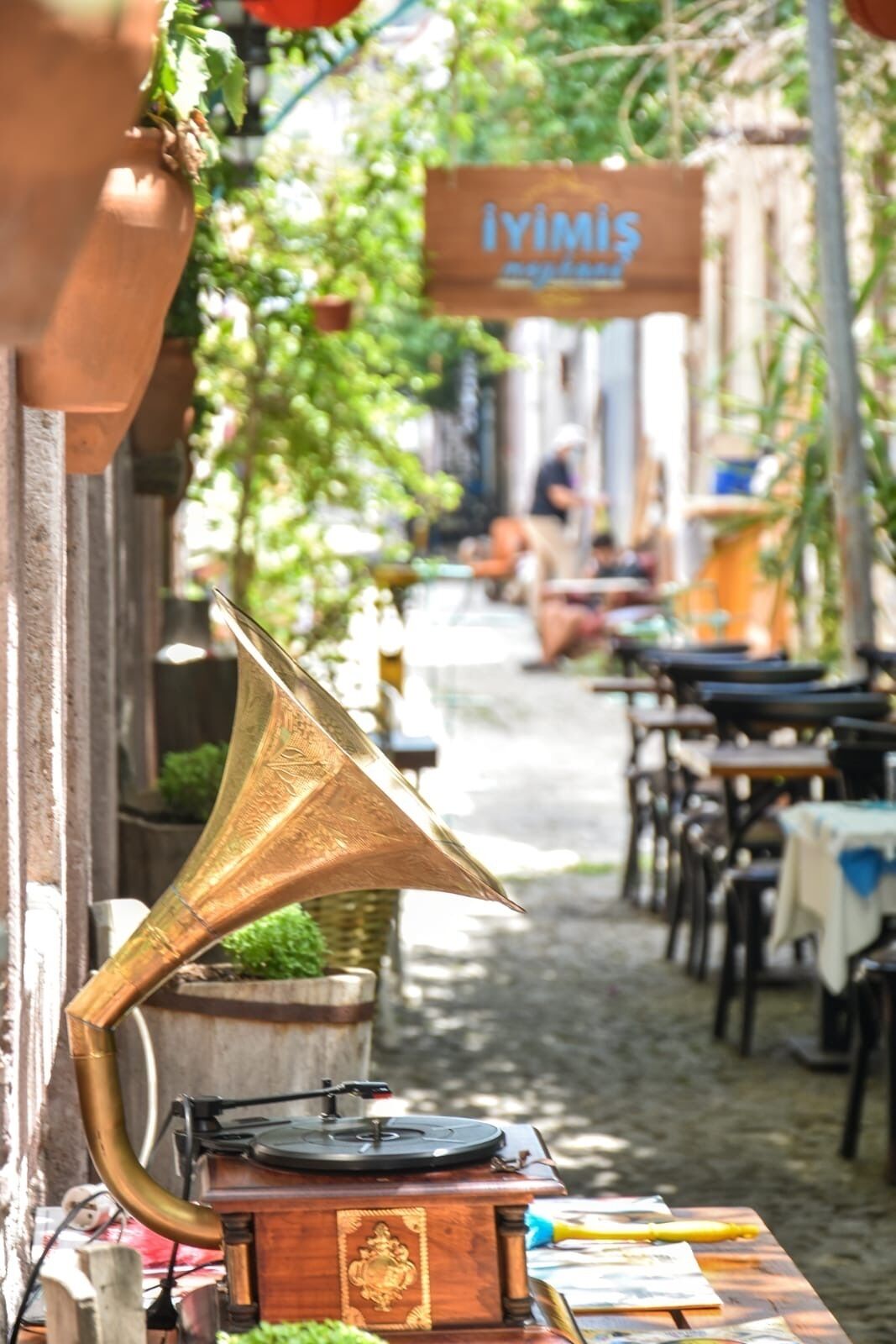 A street scene with a gramophone on a table, a sign reading "İYİMİS," and outdoor seating.