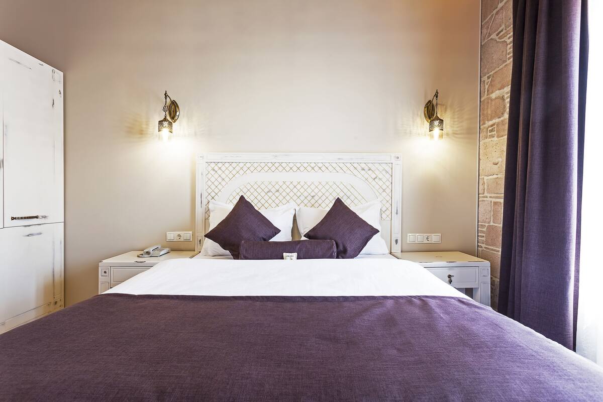 A neatly arranged hotel room with a bed, bedside tables, a telephone, and a wall-mounted light fixture.
