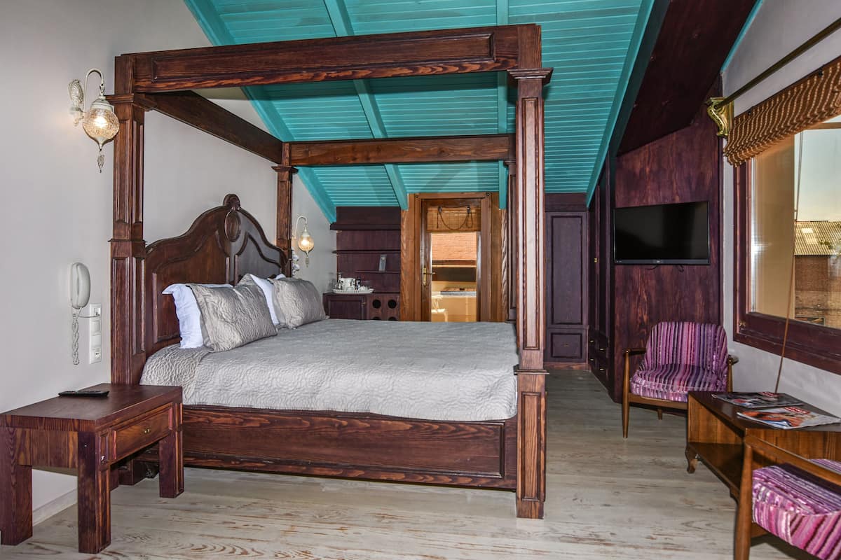 A four-poster bed with a wooden frame and a headboard, a nightstand with a lamp, a chair with a striped cushion, and a television mounted on the wall.