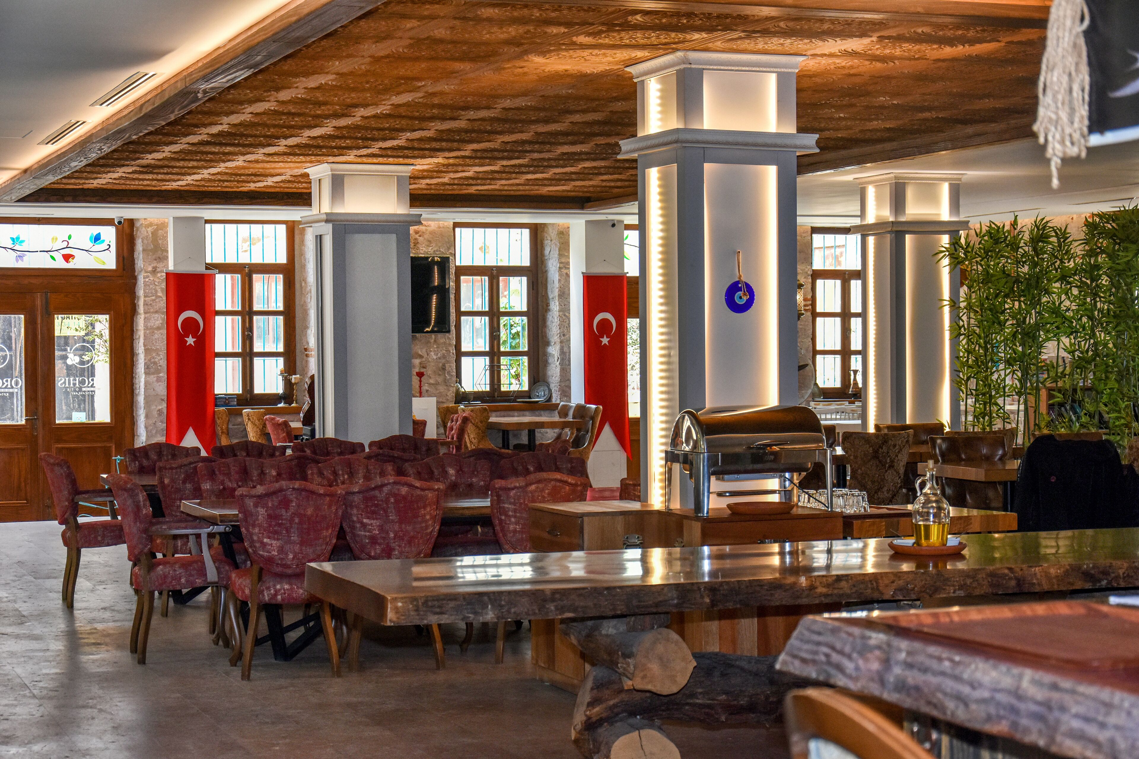 A restaurant with wooden tables and chairs, a bar area, and a large plant.