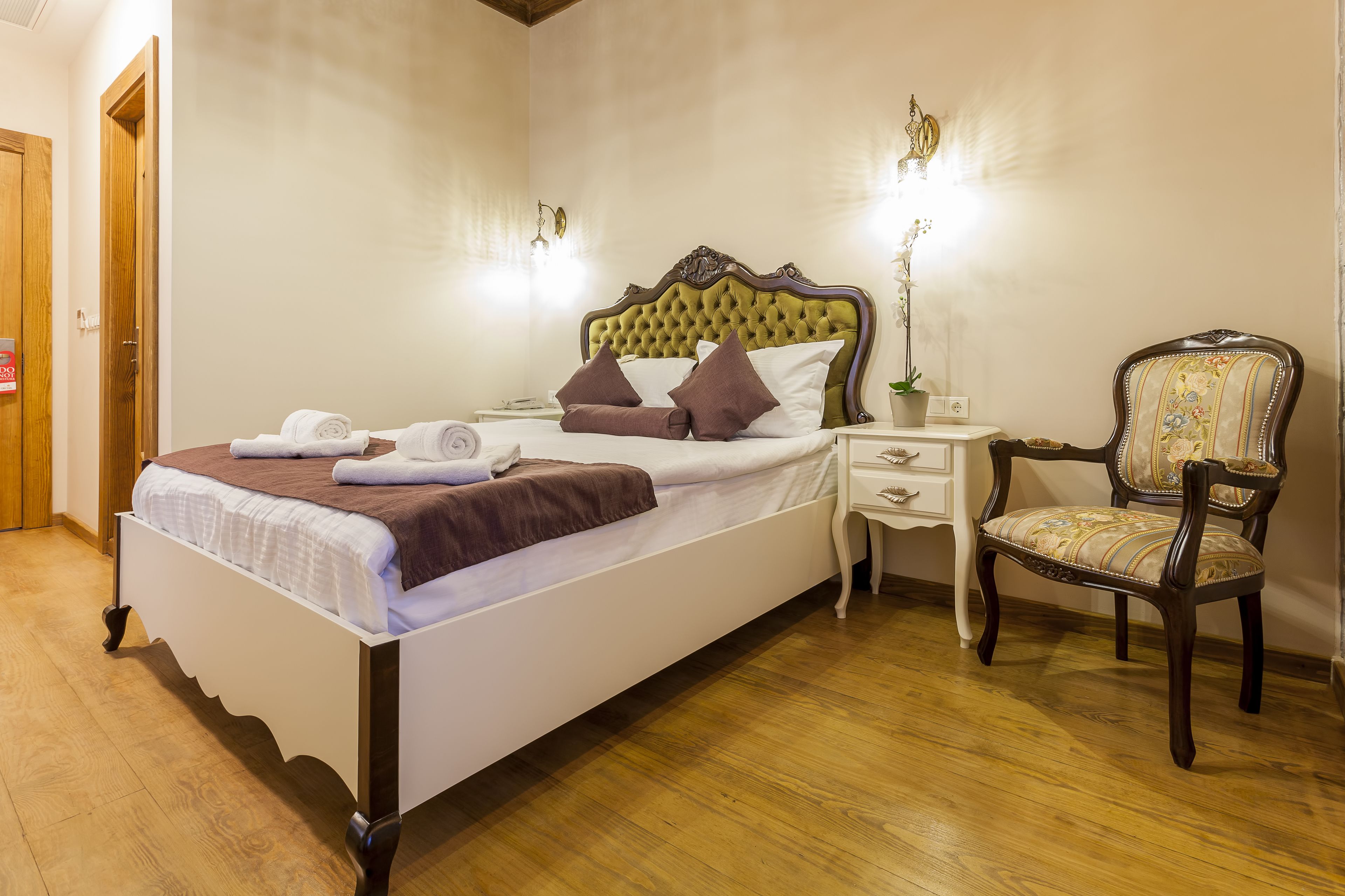 A neatly made bed with pillows and a blanket, a wooden chair with a cushion, and a bedside table with a lamp.