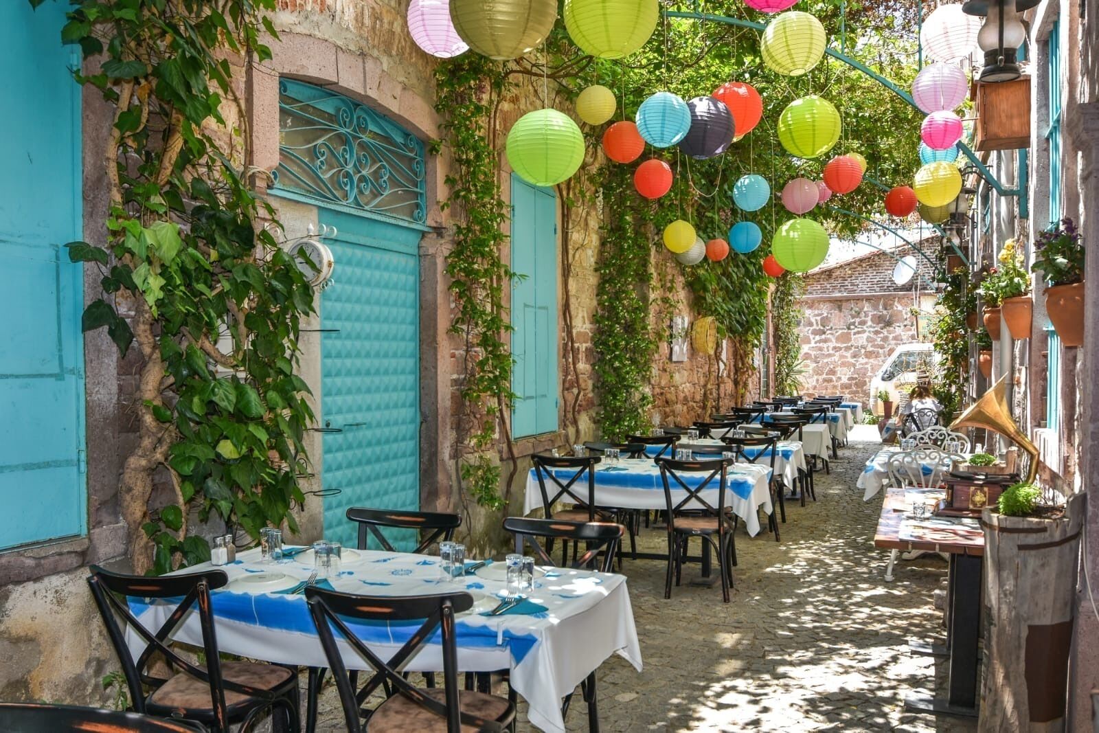 An outdoor dining area with tables set for guests, surrounded by stone walls and greenery.