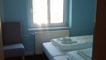 A small, simple room with a single bed, a chair, and a window.