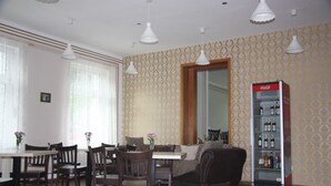 A dining area with wooden chairs and tables, a sofa, and a refrigerator stocked with beverages. - Hotel am Fluss (Heidesee)