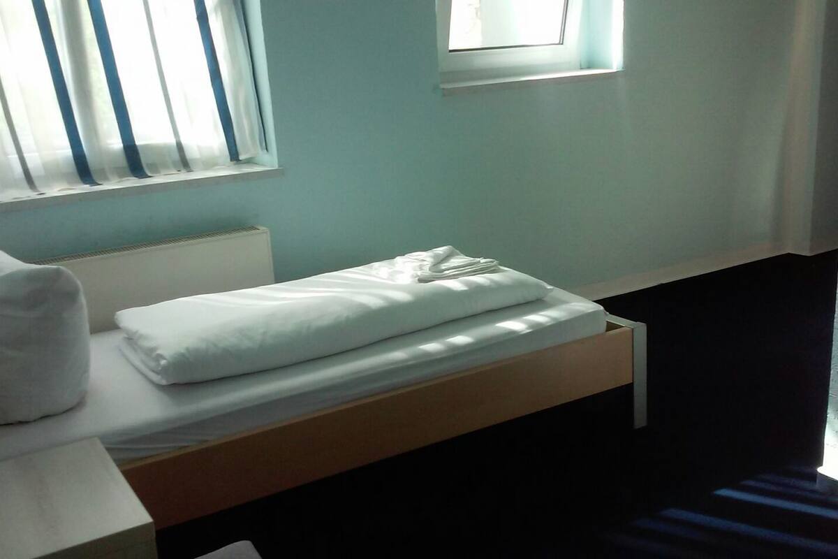 A single bed with white bedding, a pillow, and a bedside table with a lamp.