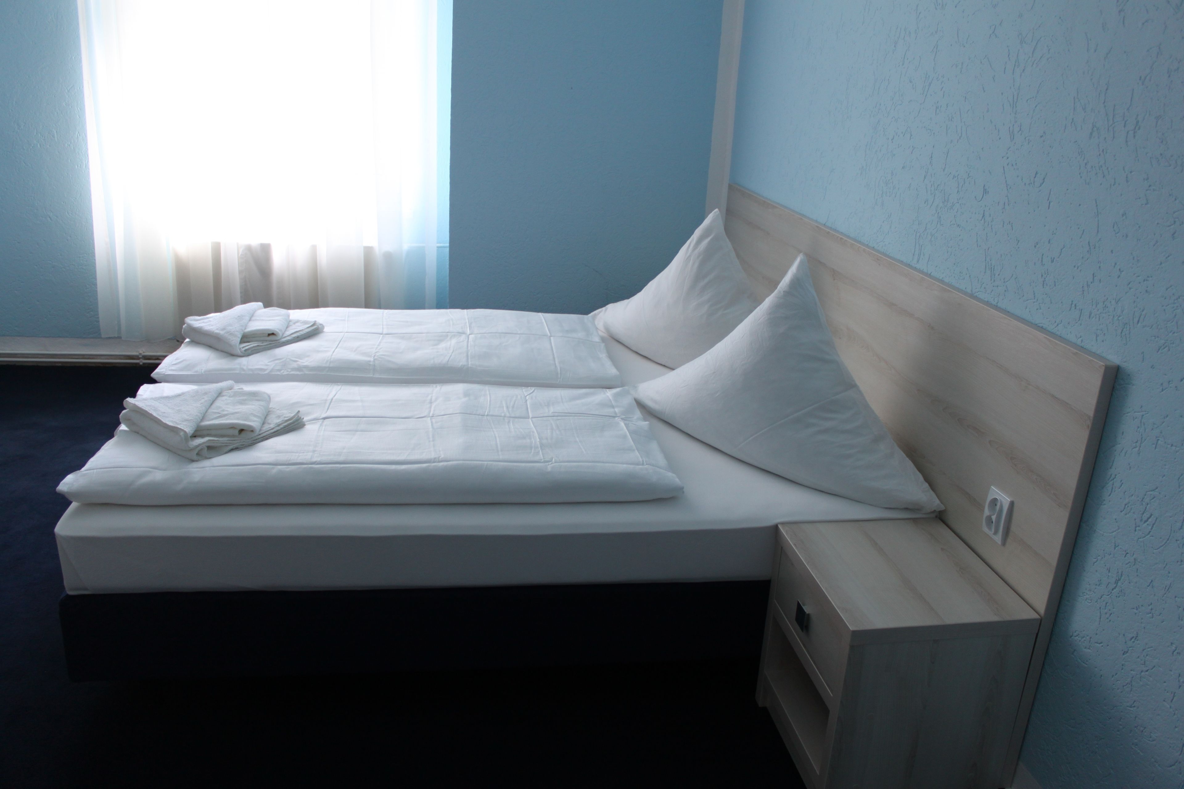 A double bed with white linens and pillows, a wooden headboard, and a nightstand with a drawer.