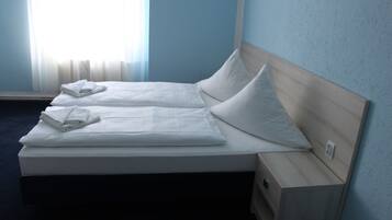 Una cama doble con sábanas y almohadas blancas, un cabecero de madera y una mesita de noche con un cajón.