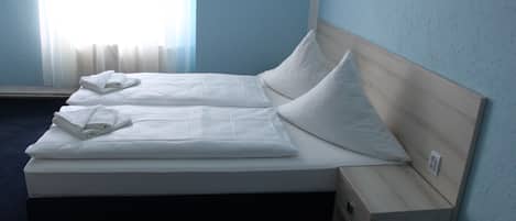 A double bed with white linens and pillows, a wooden headboard, and a nightstand with a drawer.