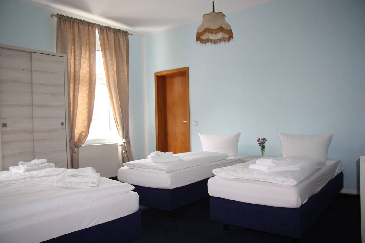 A hotel room with two beds, a wooden door, and a window with curtains.