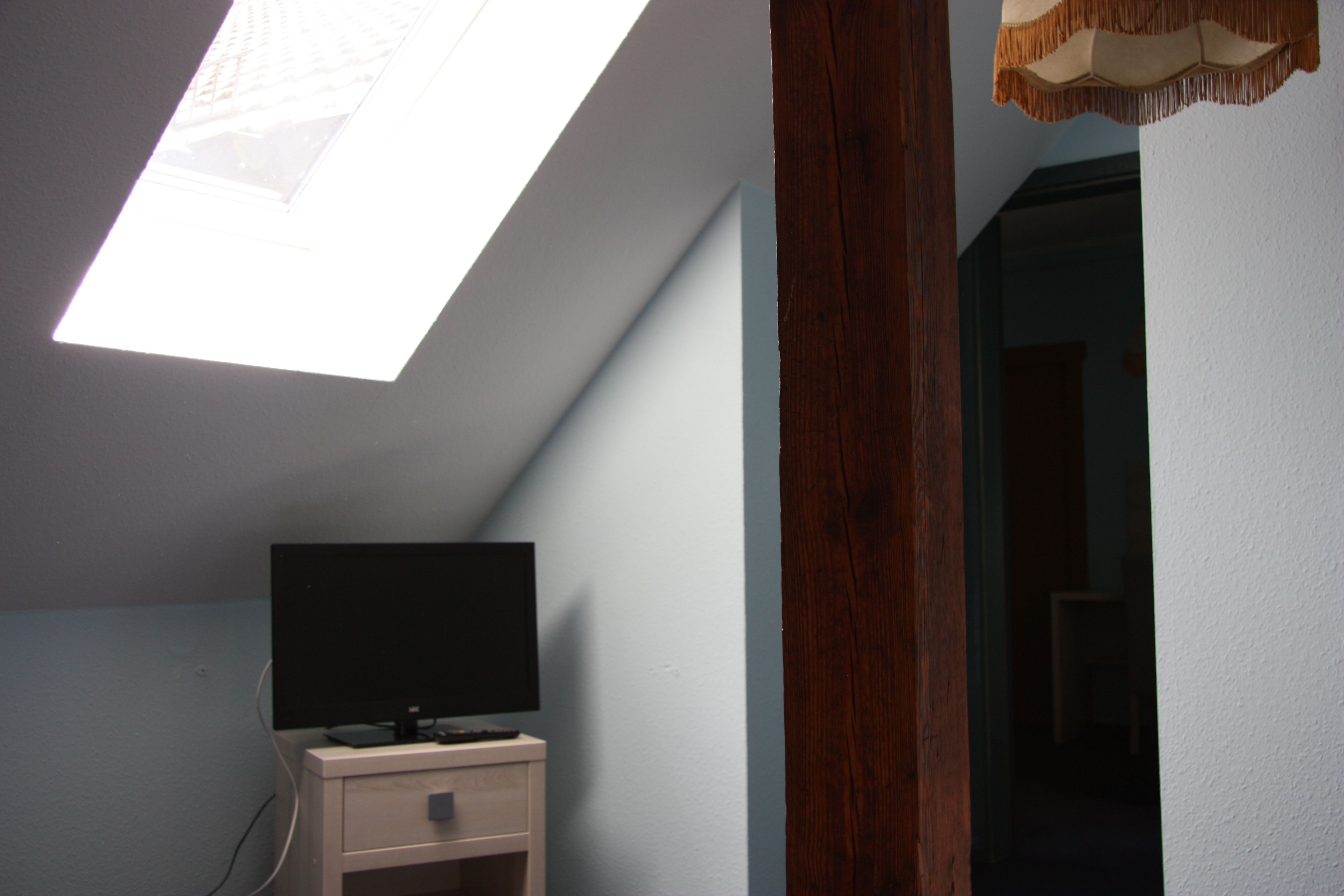 Una habitación con tragaluz, un televisor sobre un mueble de madera y un acceso a otra habitación.