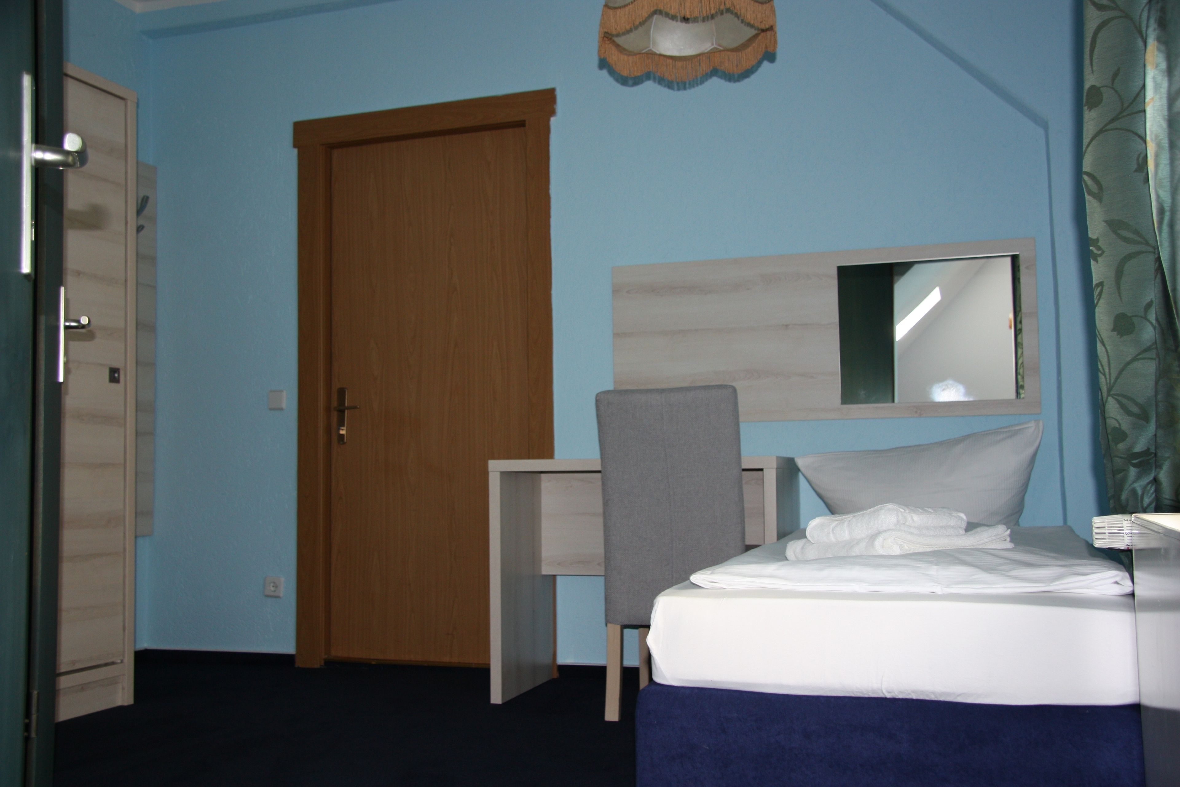 Quarto de hotel com cama, escrivaninha, cadeira, guarda-roupa e espelho na parede.