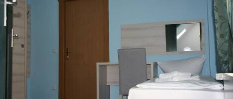 Quarto de hotel com cama, escrivaninha, cadeira, guarda-roupa e espelho na parede.