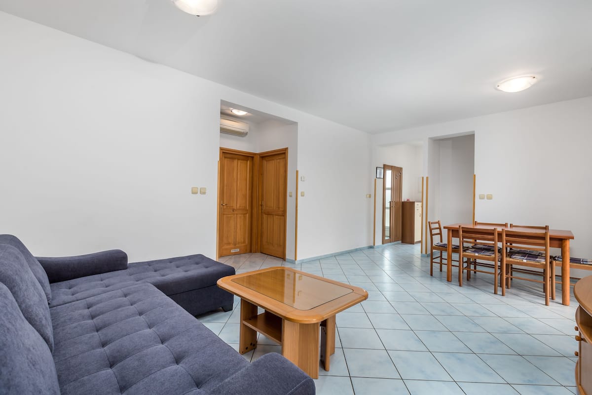 Uma sala de estar moderna com um sofá, uma mesa de centro de vidro e uma área de jantar com mesa e cadeiras de madeira.