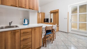 A kitchen with wooden cabinets, a sink, a kettle, and a dining area with chairs and a table. - Apartments Gea (Moscenicka Draga)