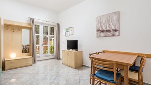 A room with a wooden dining table, chairs, a TV on a cabinet, a bench with drawers, and a large window with curtains. - Apartments Gea (Moscenicka Draga)