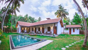 Une maison à deux étages avec une piscine, entourée de palmiers et d’une pelouse bien entretenue.