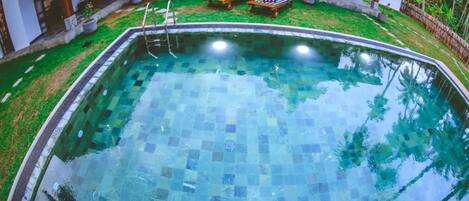 Una piscina con mosaicos, rodeada de césped y sillas de descanso.