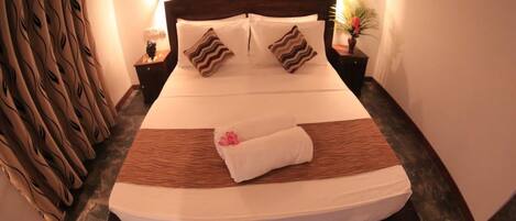 A neatly made bed with a wooden headboard, two pillows, and a rolled towel.