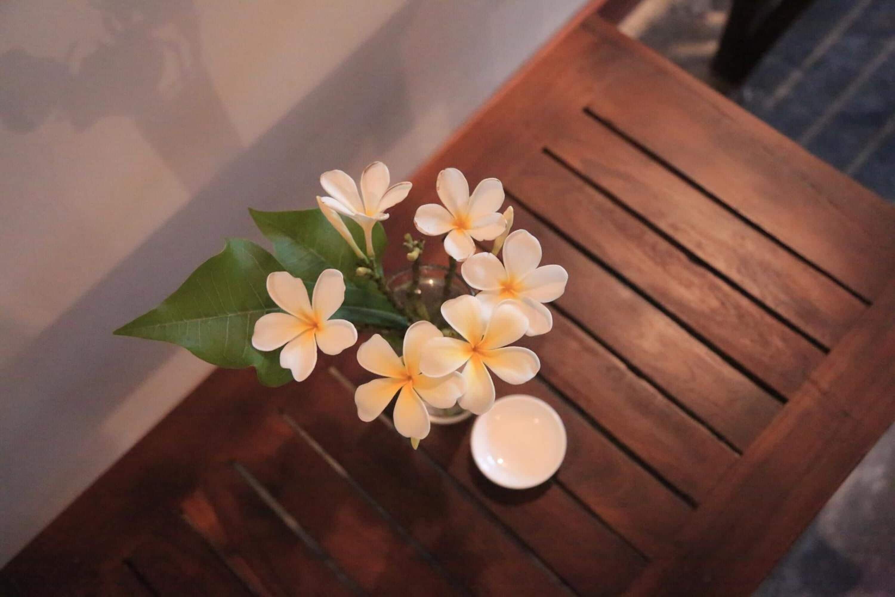 Een houten tafel met een vaas vol witte bloemen en een kaarsje.