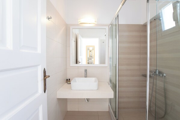 A modern bathroom with a glass shower enclosure, a white sink, and a mirror above it. - Agia Anna on the beach (Mykonos)