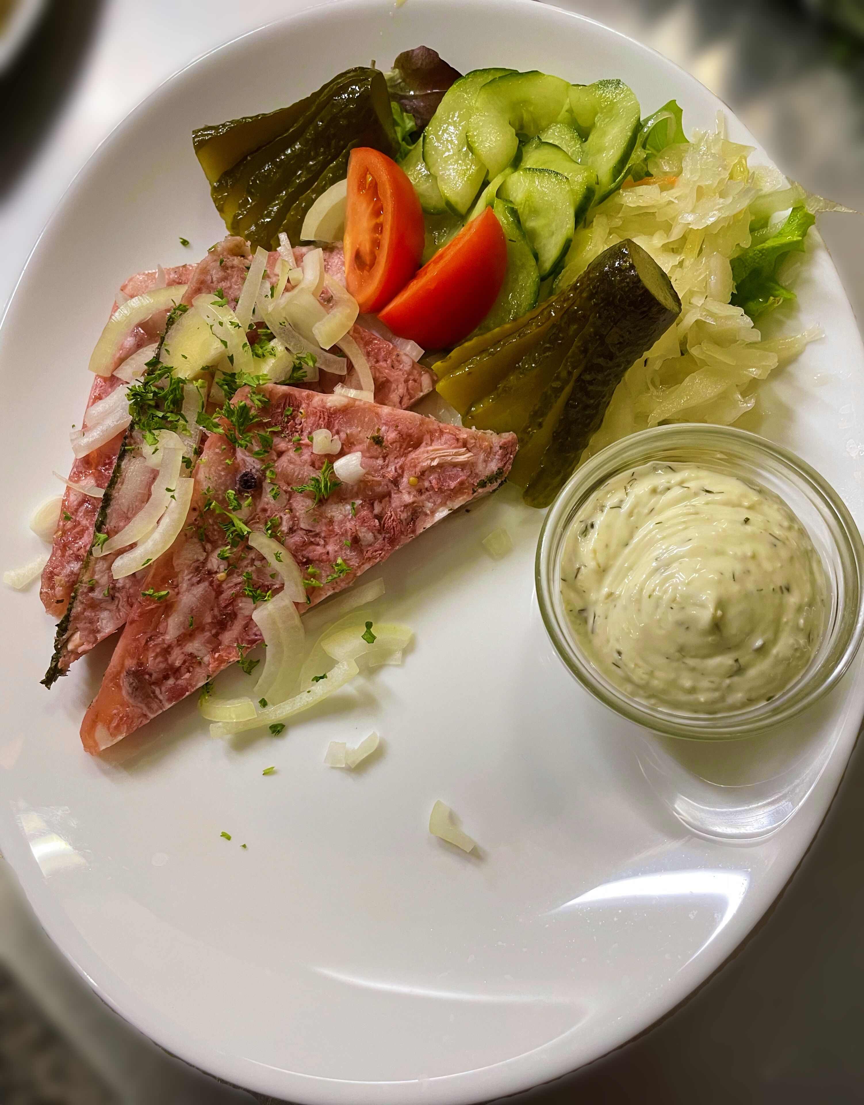 A plate with sliced meat, vegetables, and a small bowl of sauce.