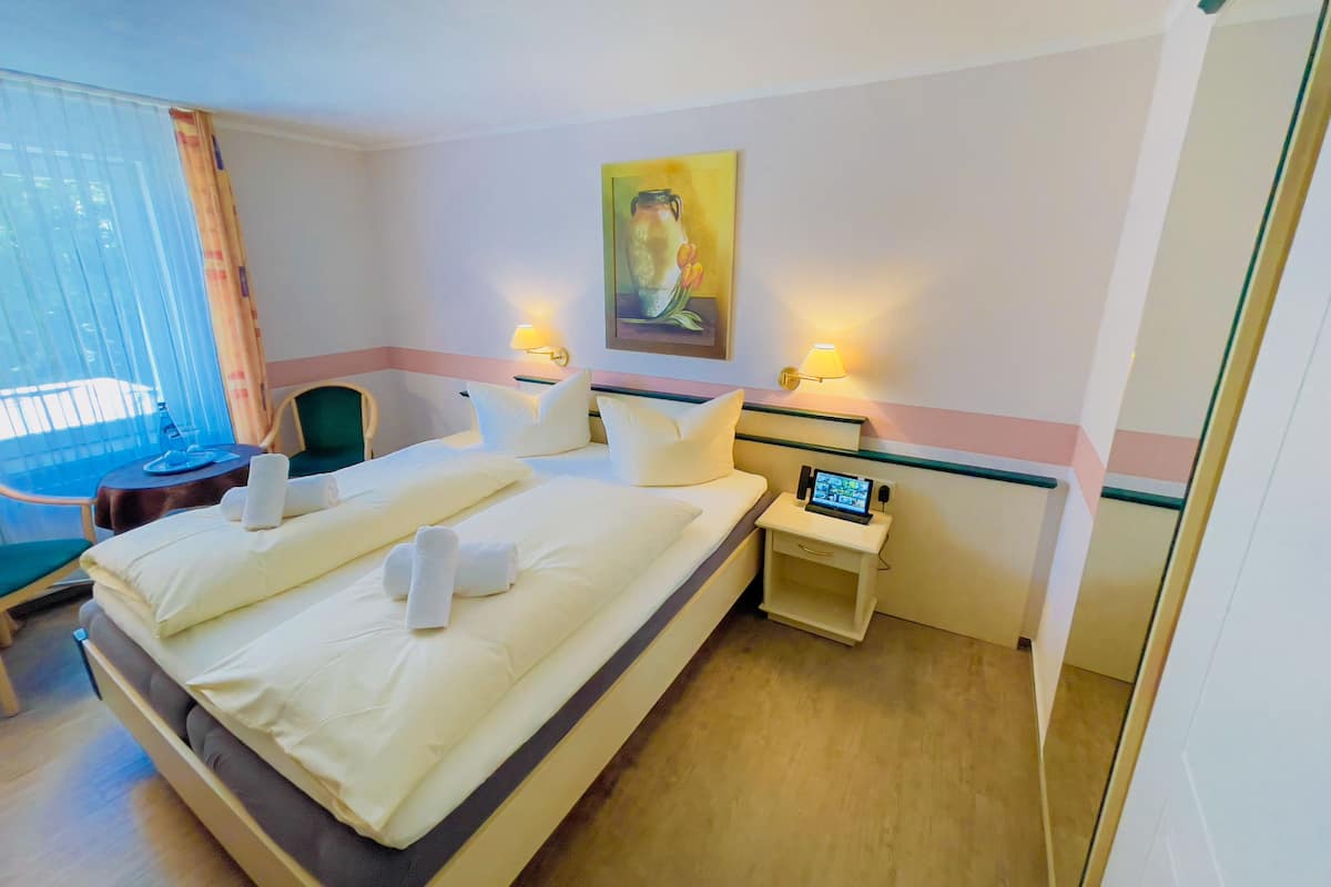 Quarto de hotel com cama, duas mesas de cabeceira, uma cadeira e uma janela com cortinas.
