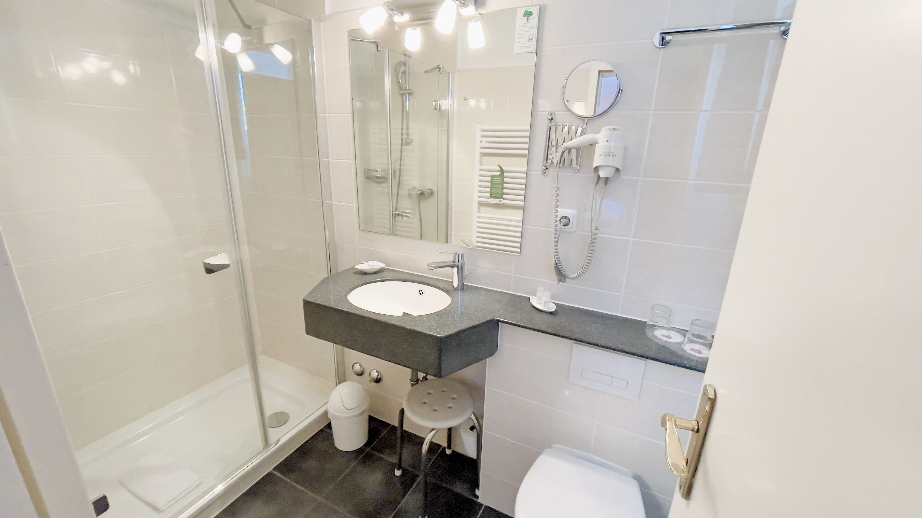 Un baño moderno con cabina de ducha de vidrio, un lavabo con tocador, inodoro y secador de pelo montado en la pared.