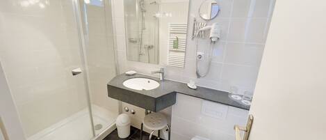 A modern bathroom with a glass shower enclosure, a sink with a vanity, a toilet, and a hairdryer mounted on the wall.