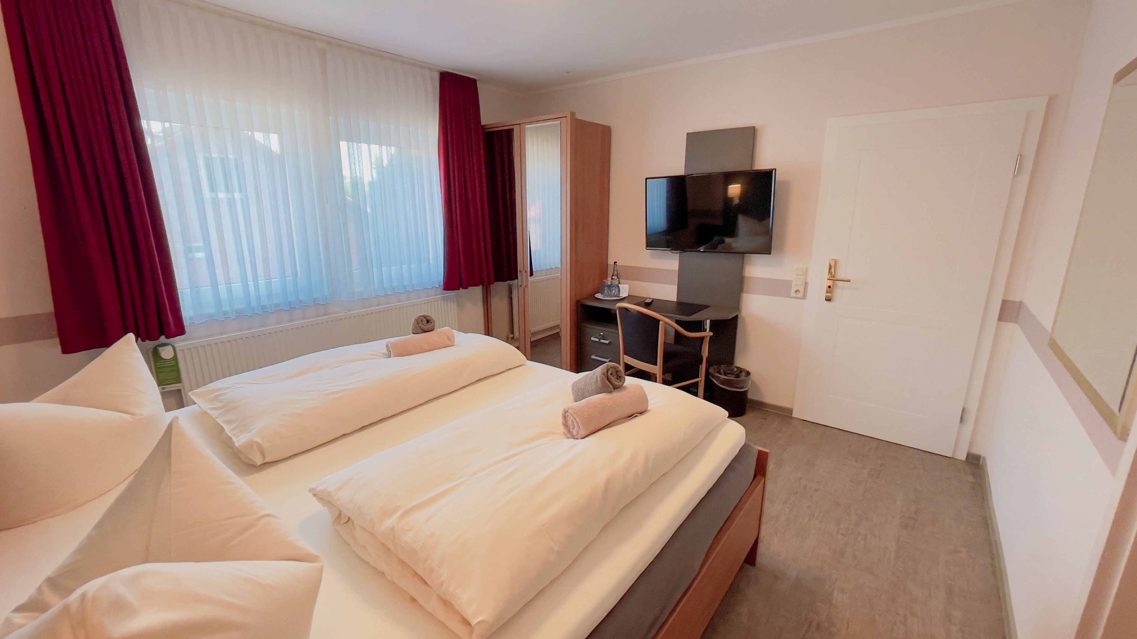 Ein Hotelzimmer mit zwei Betten, einem Schreibtisch, einem Fernseher und einer Tür.