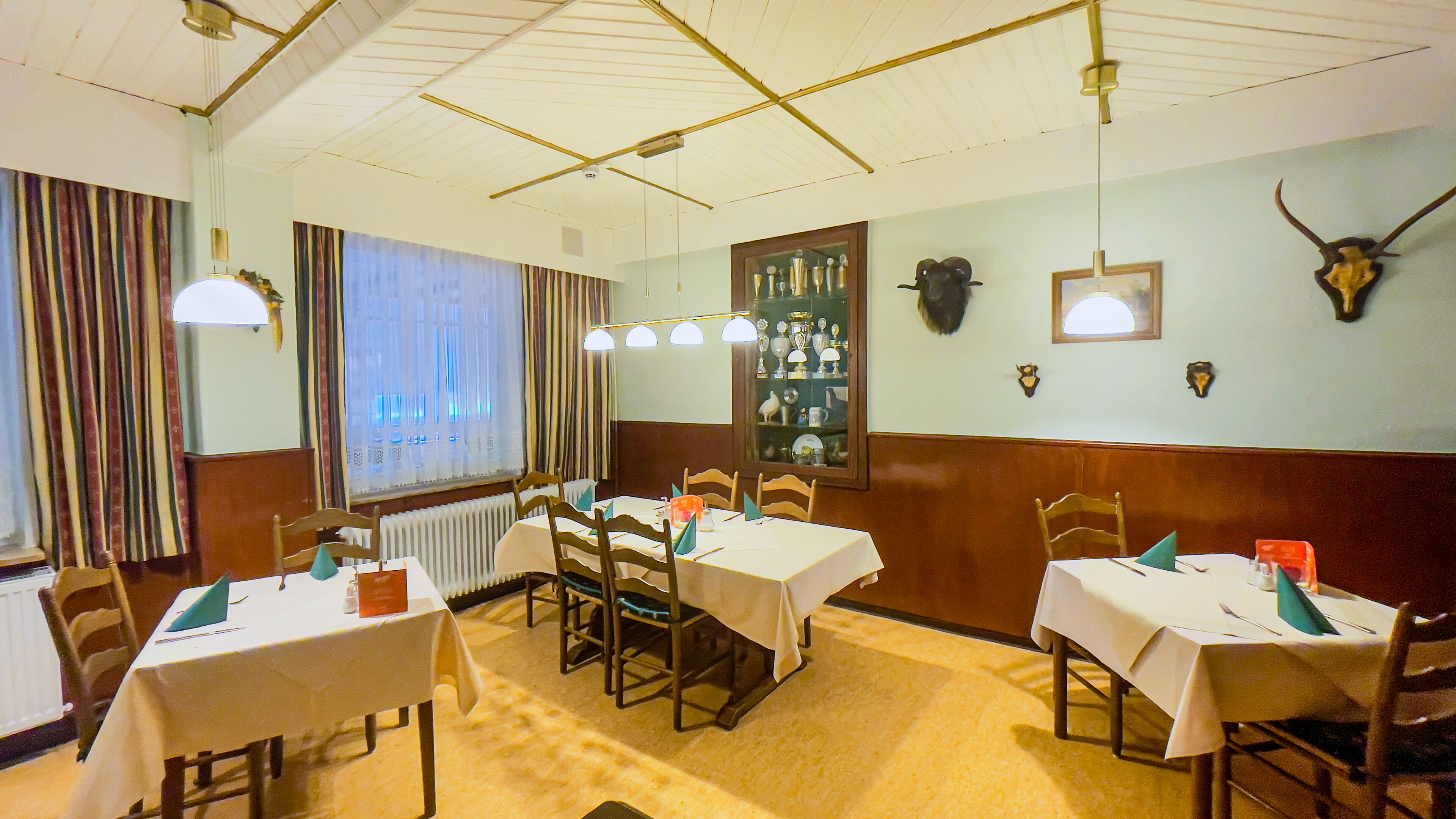 A dining area with tables set for service, a display of trophies, and animal horns on the wall.