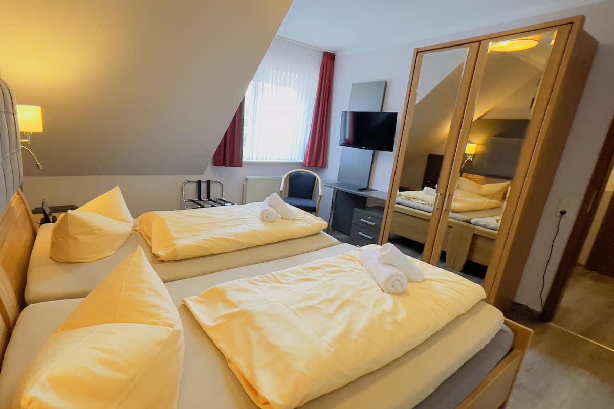 Quarto de hotel com duas camas, uma escrivaninha, uma cadeira, uma televisão e um espelho.