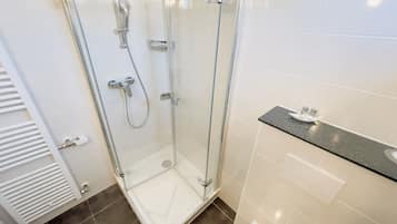 Un baño moderno con ducha de vidrio, azulejos blancos y una encimera con artículos de aseo.