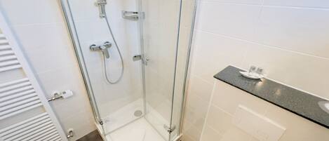 Un baño moderno con ducha de vidrio, azulejos blancos y una encimera con artículos de aseo.