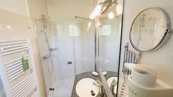 A modern bathroom with a glass-enclosed shower, a white sink, and a round mirror.